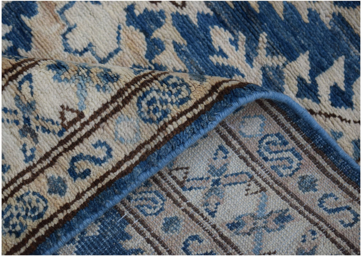 A folded Afghan Super Kazakh runner featuring traditional blue and cream geometric patterns.