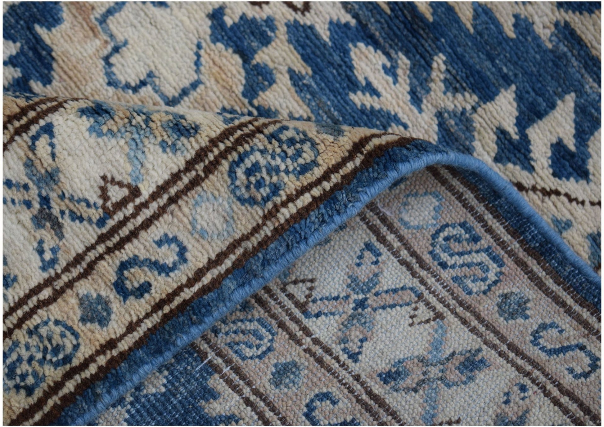A folded Afghan Super Kazakh runner featuring traditional blue and cream geometric patterns.