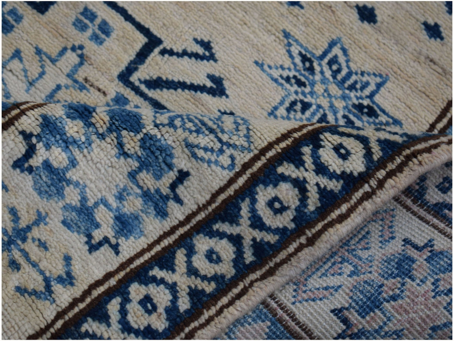 A folded Afghan Super Kazakh runner featuring traditional blue and cream geometric patterns.