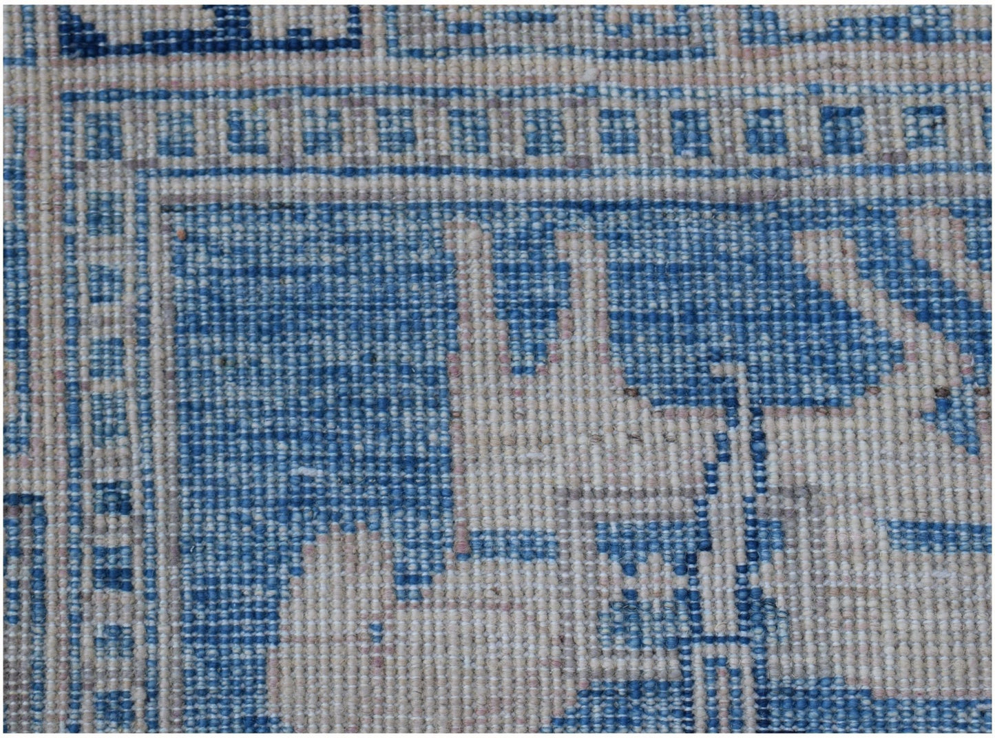 A close-up of an Afghan Chobi rug featuring intricate blue and cream geometric patterns.