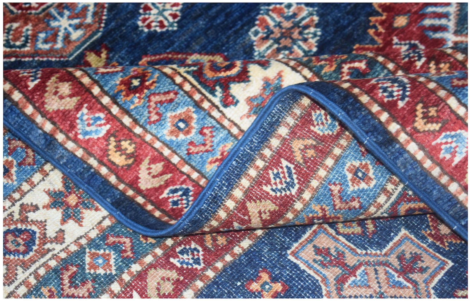 A folded Afghan Super Kazakh rug featuring traditional geometric patterns in blue, red, and cream.