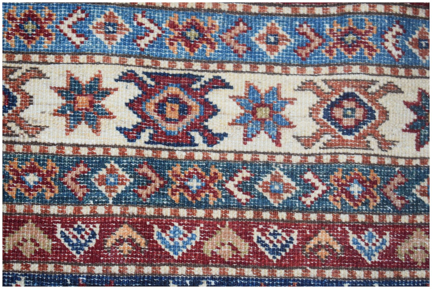 A close-up of an Afghan Super Kazakh rug featuring traditional geometric patterns in blue and red.