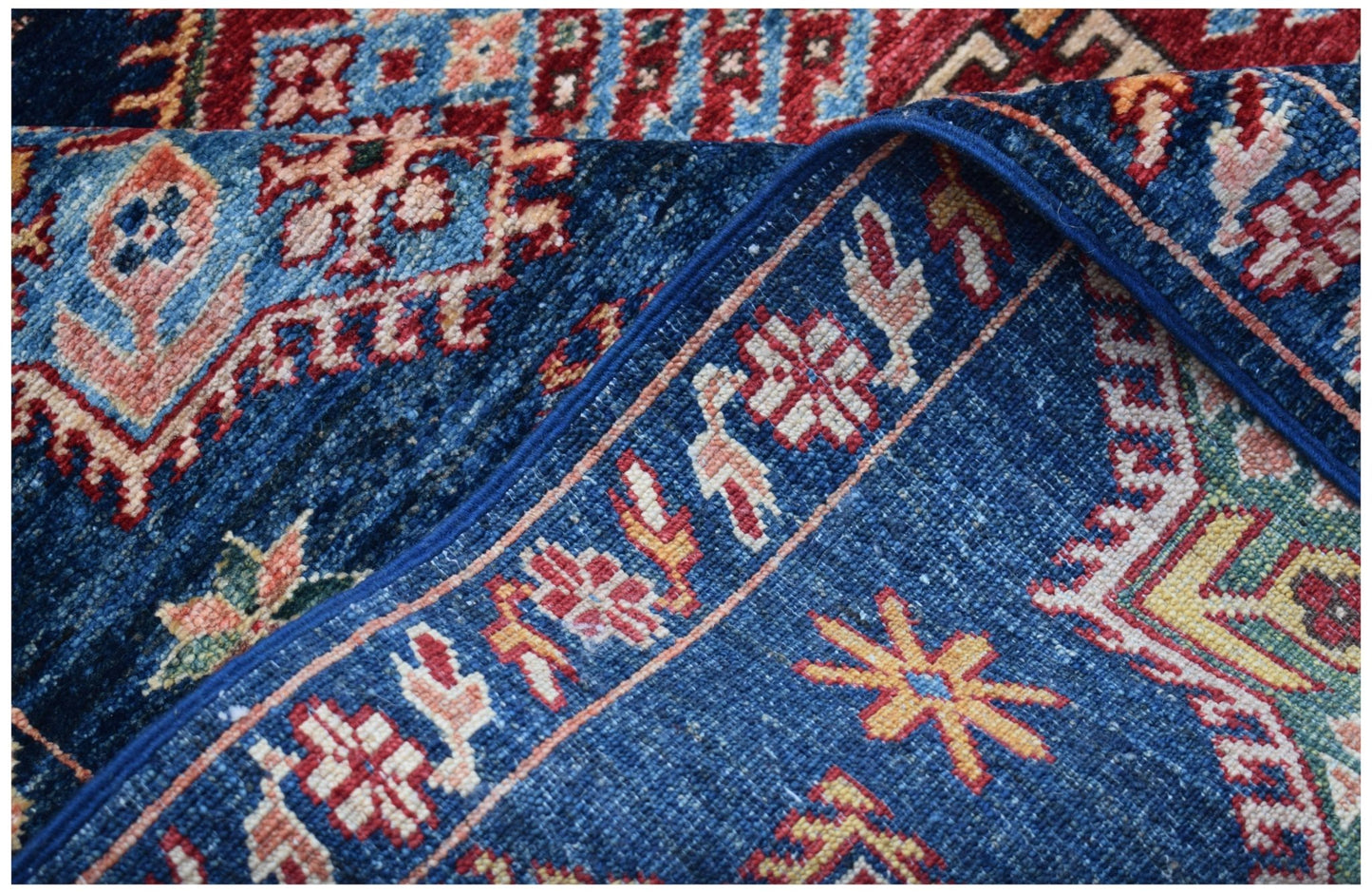 A close-up of a handmade Afghan Kazakh rug featuring traditional geometric patterns in blue and red.