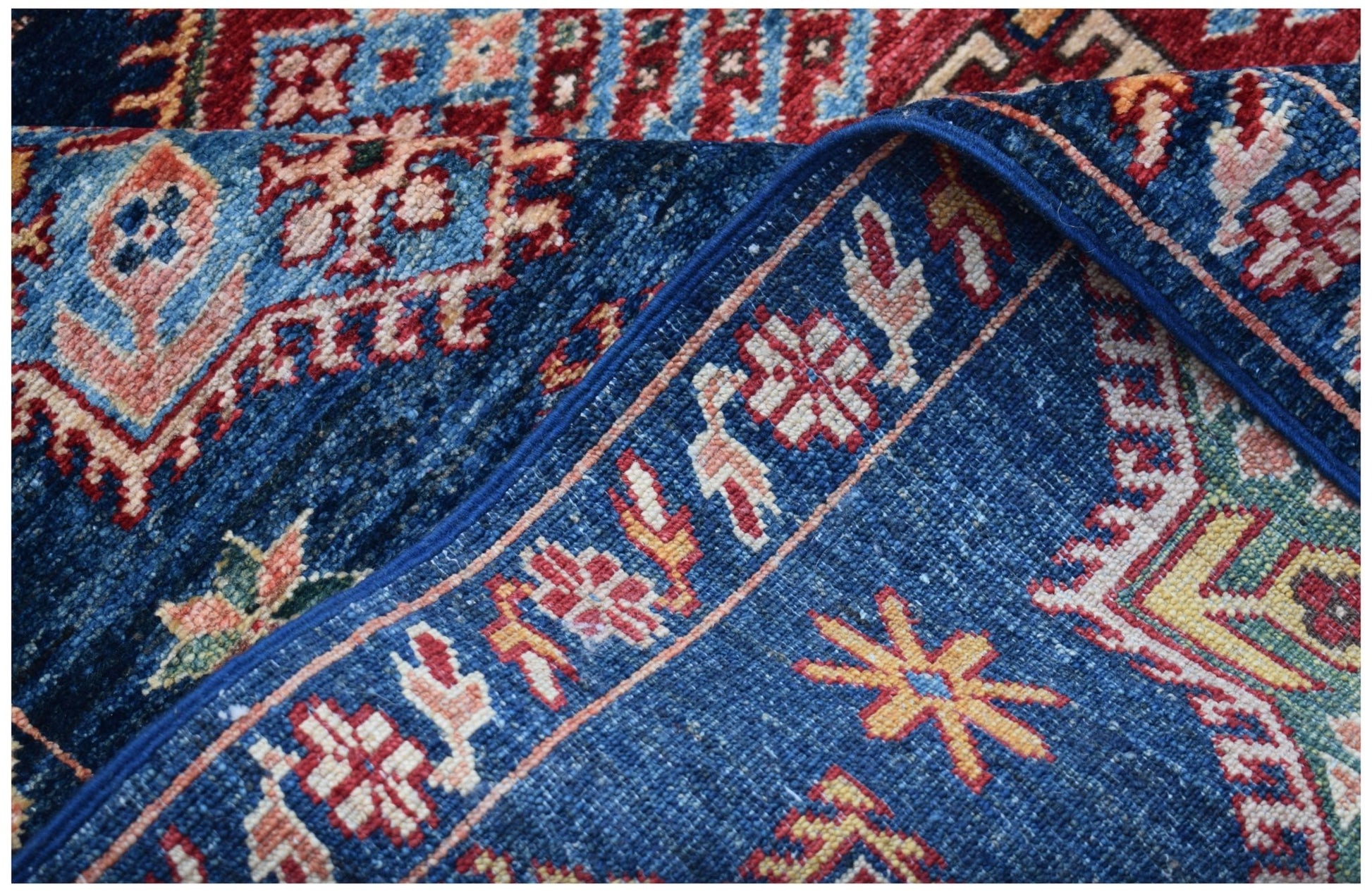 A close-up of a handmade Afghan Kazakh rug featuring traditional geometric patterns in blue and red.