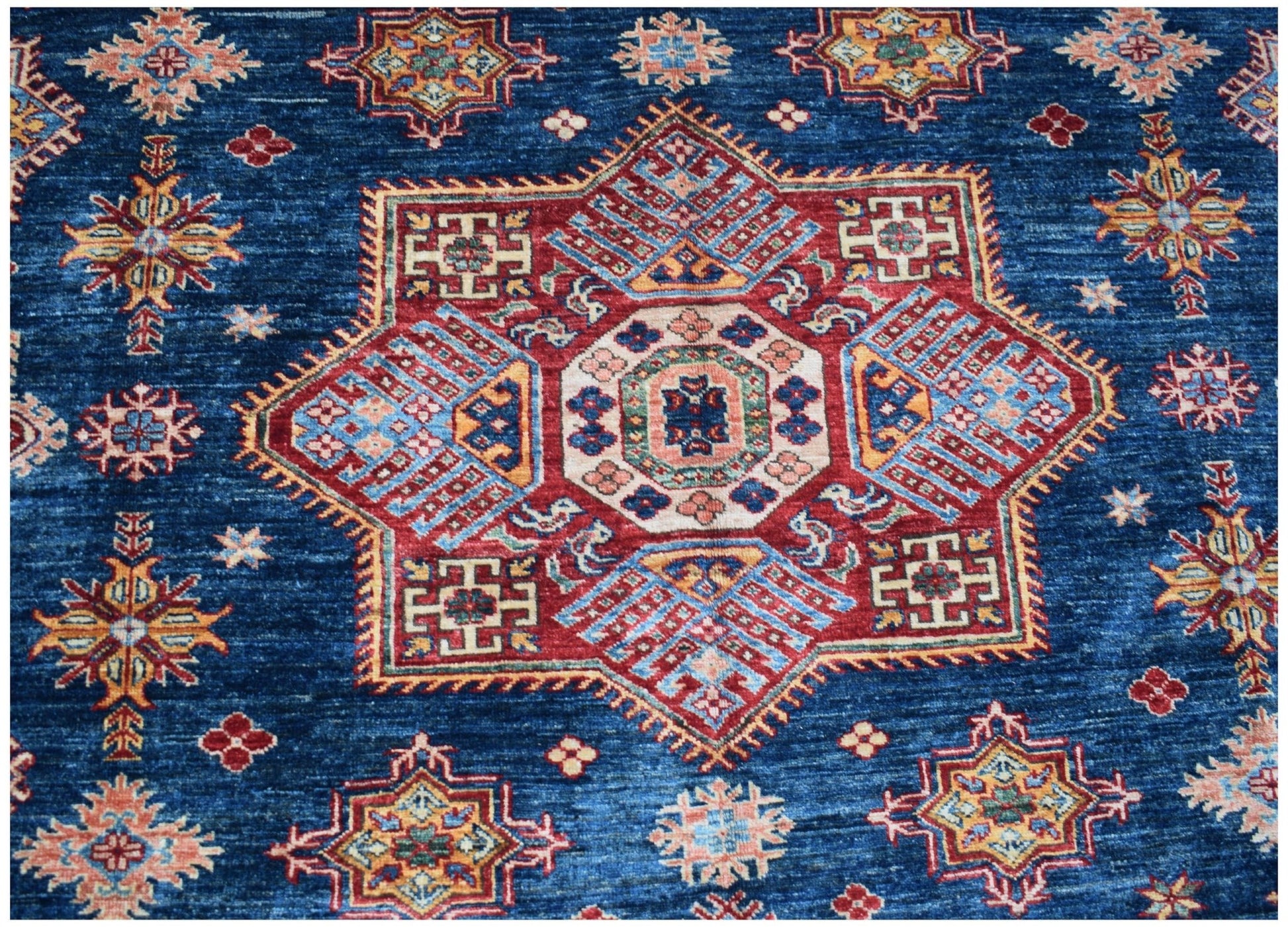 A handmade Afghan Kazakh rug featuring a large central star medallion on a deep blue field.