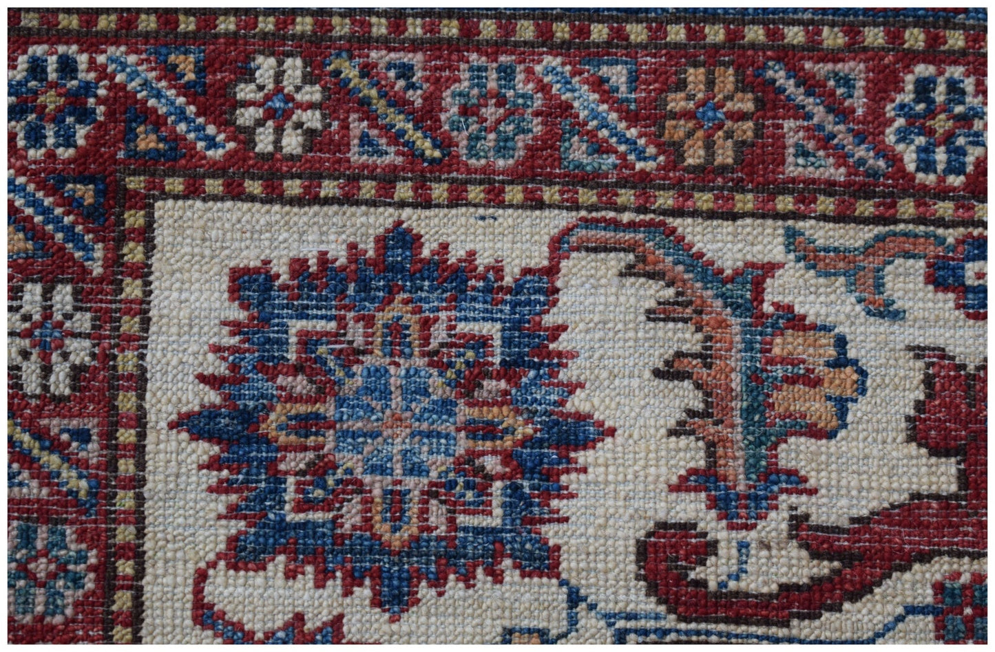 A close-up of an Afghan Super Kazakh rug featuring traditional floral motifs in red and blue.
