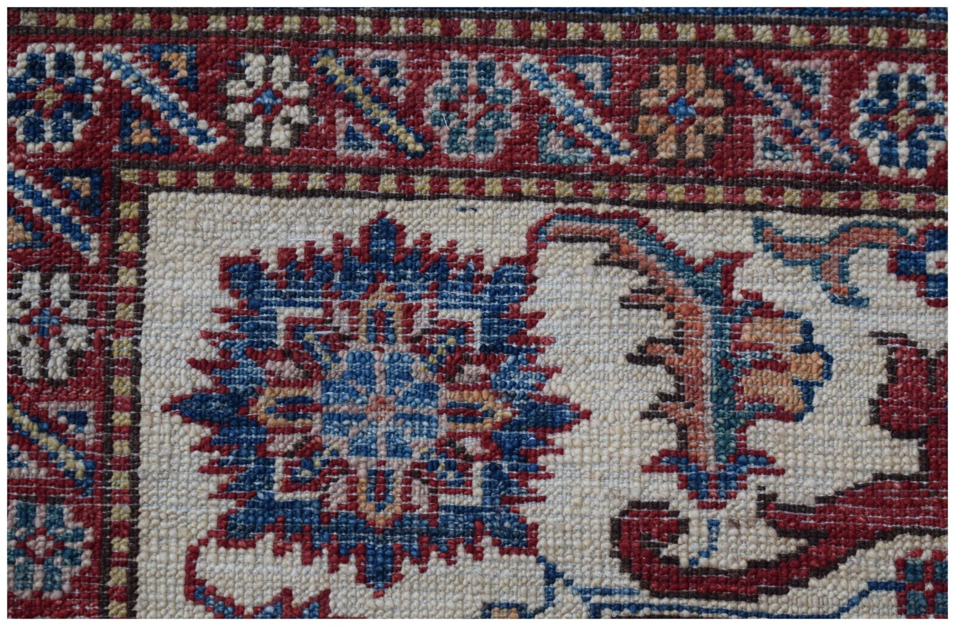 A close-up of an Afghan Super Kazakh rug featuring traditional floral motifs in red and blue.