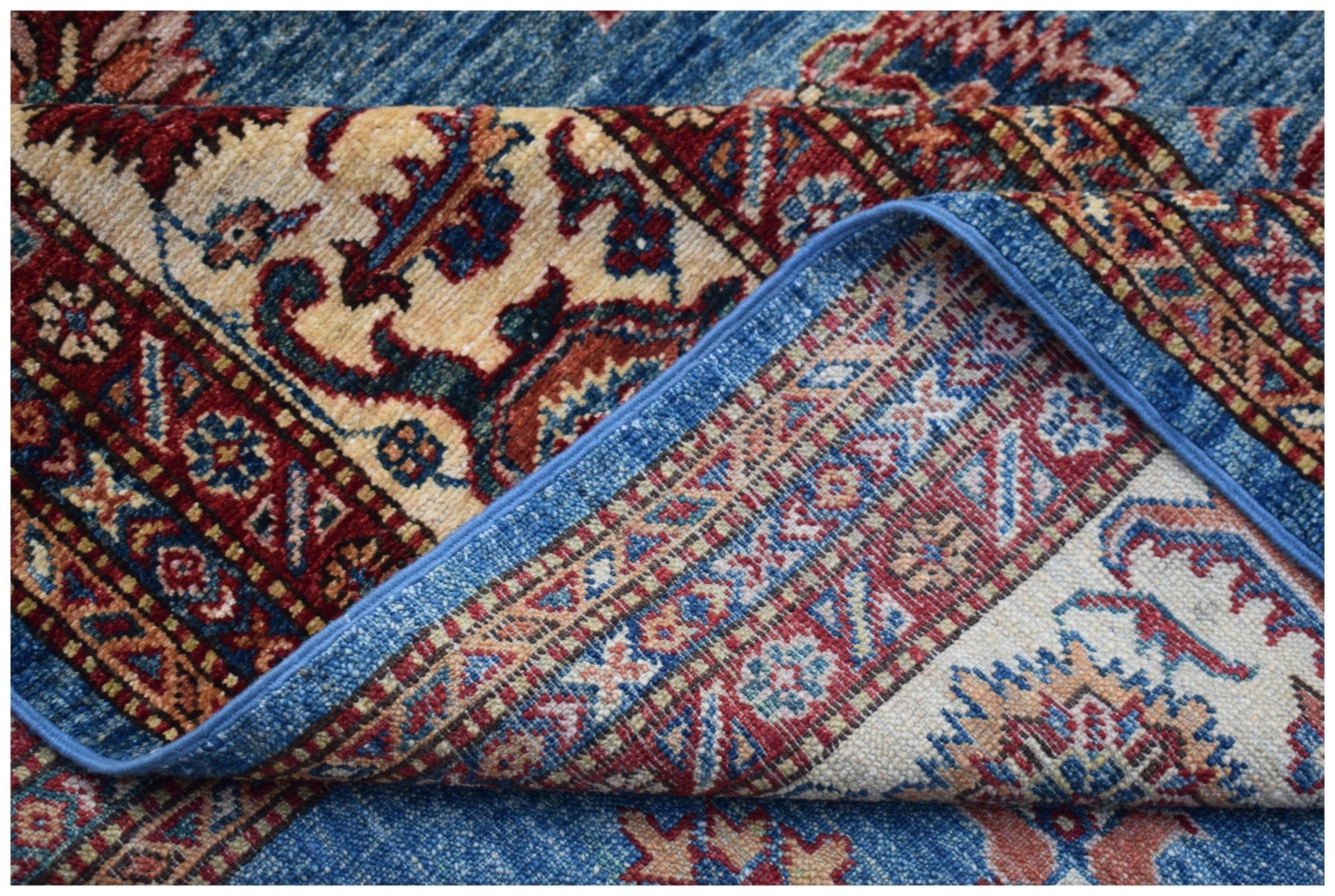 A corner of a handmade Afghan Super Kazakh rug showing its intricate floral patterns and wool weave.
