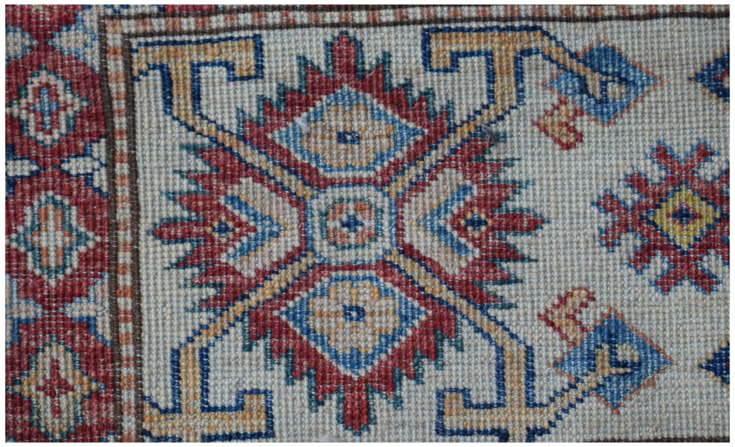 A close-up of an Afghan Super Kazakh rug featuring a traditional geometric medallion in red and blue.