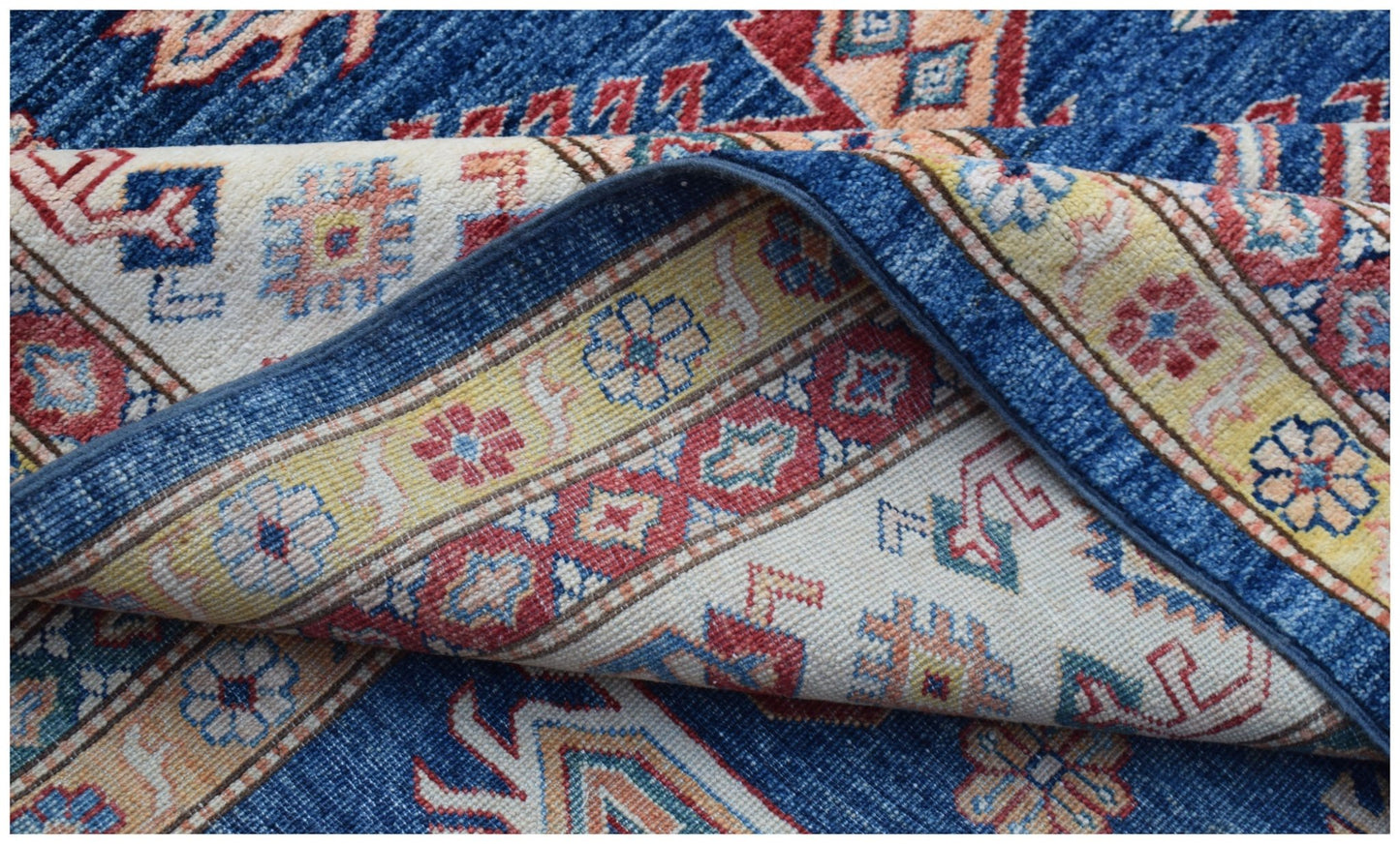 A folded Afghan Super Kazakh rug featuring traditional geometric patterns in blue, red, and yellow.