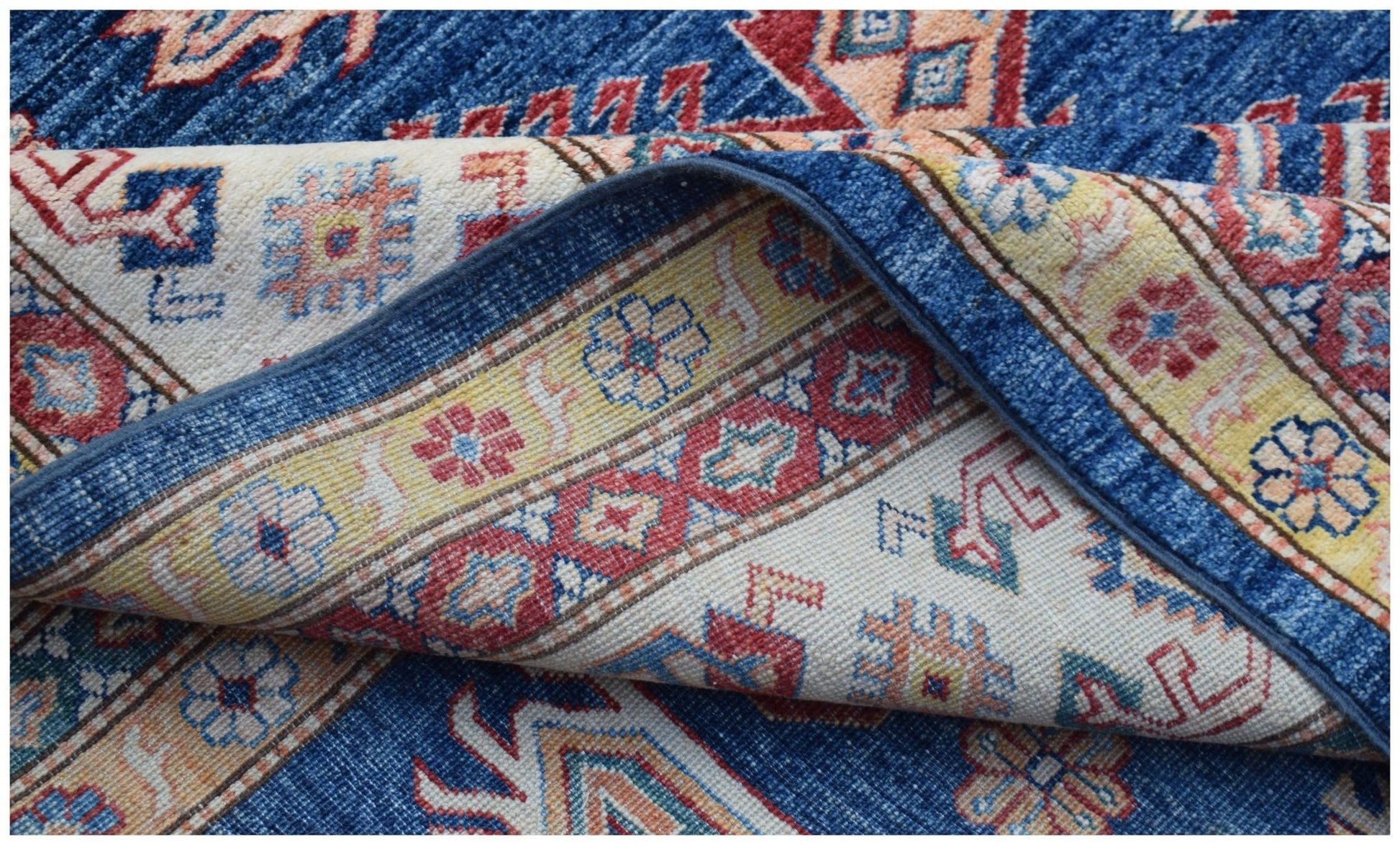 A folded Afghan Super Kazakh rug featuring traditional geometric patterns in blue, red, and yellow.