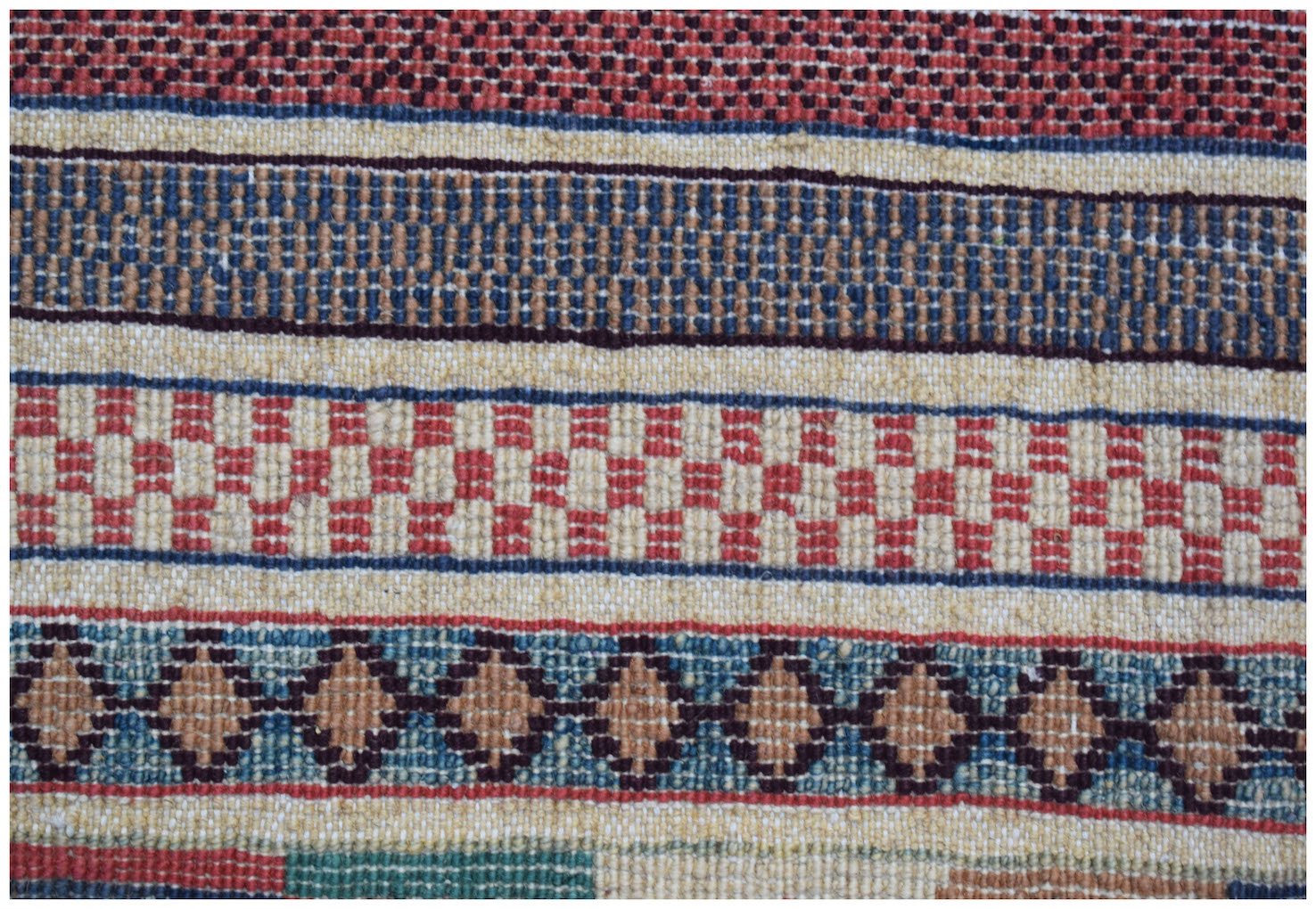 A handmade Afghan runner featuring horizontal bands of geometric patterns in red, blue, and tan.