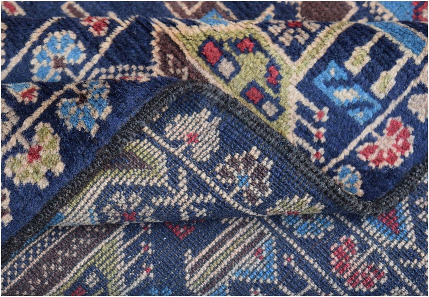 A folded handmade Afghan wool rug featuring intricate geometric and floral patterns in blue.