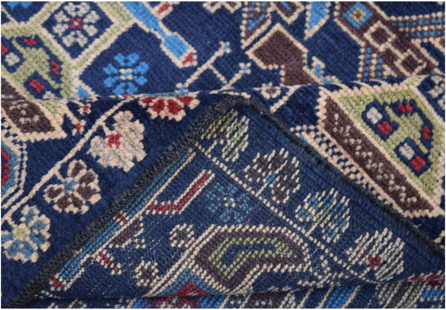 A corner of a handmade Afghan wool rug featuring intricate geometric patterns in blue and brown.
