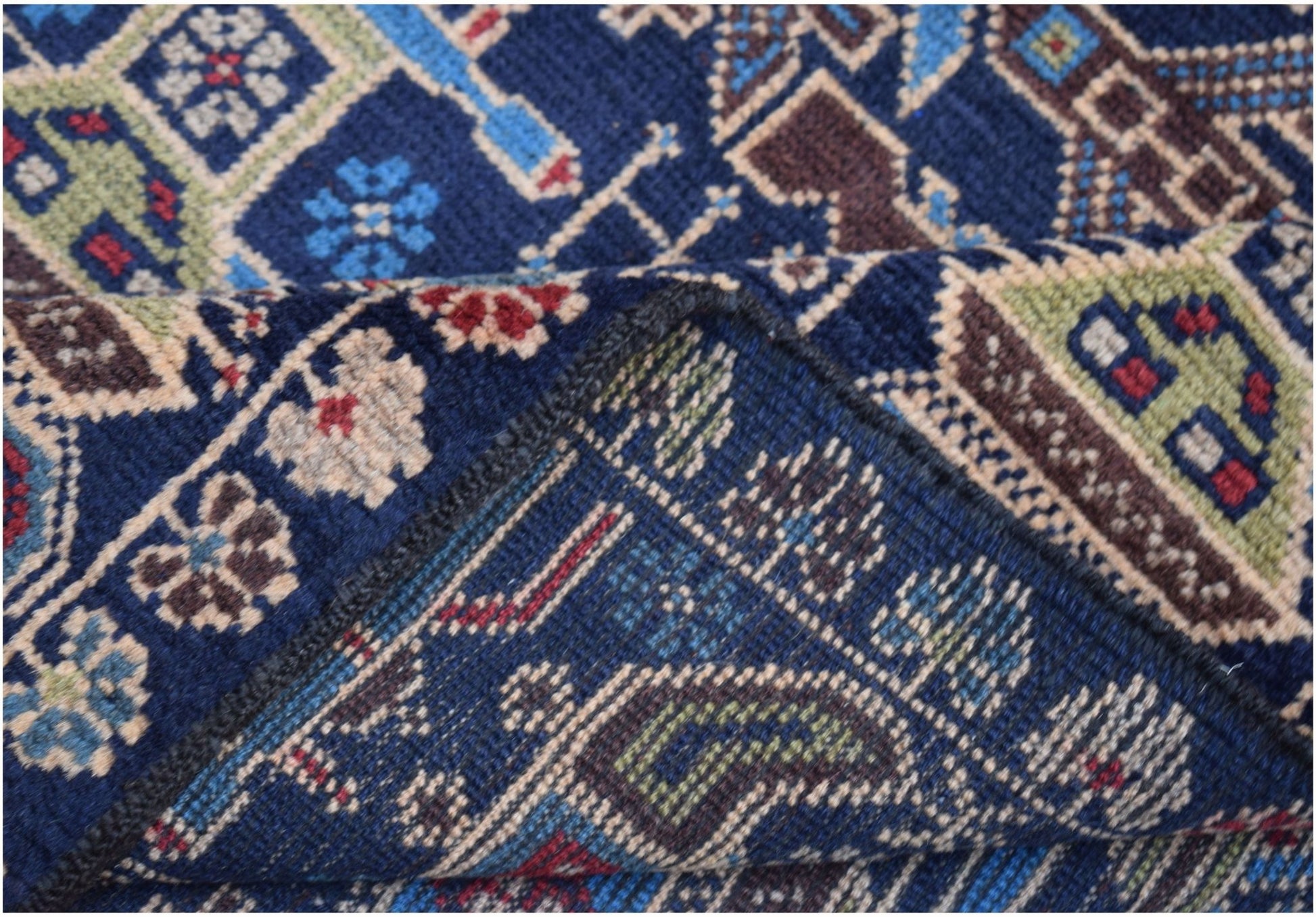 A corner of a handmade Afghan wool rug featuring intricate geometric patterns in blue and brown.