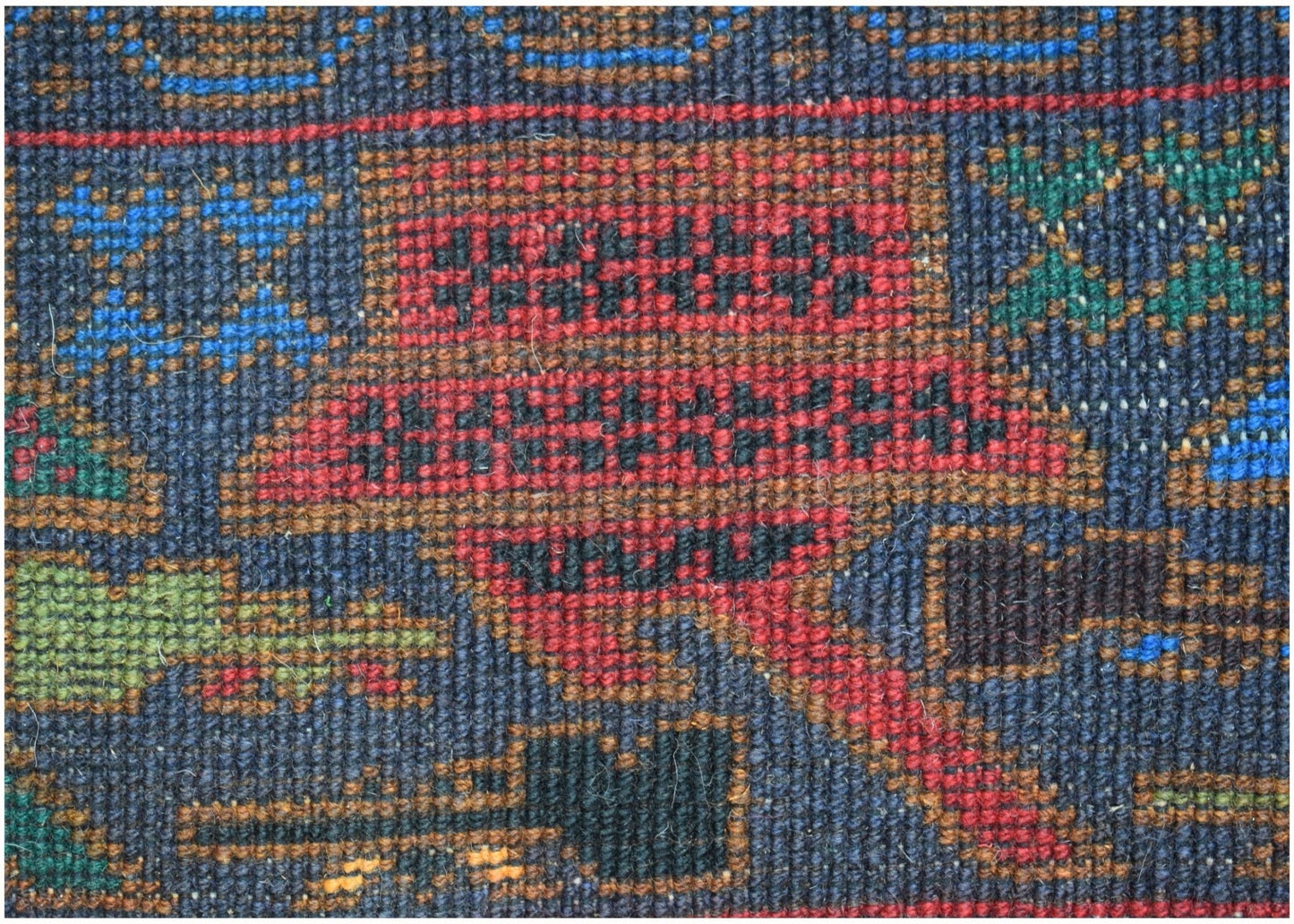 A close-up of a handmade Afghan wool rug featuring geometric patterns in red, blue, and green.