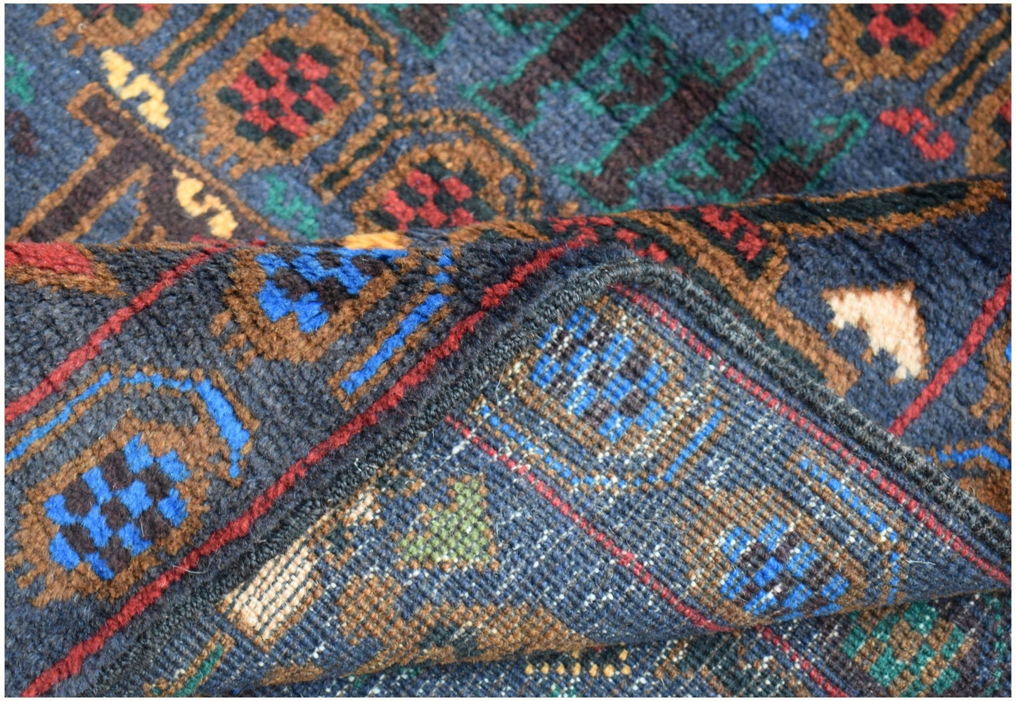 A close-up of a handmade Afghan wool rug featuring geometric patterns in blue, red, and brown.