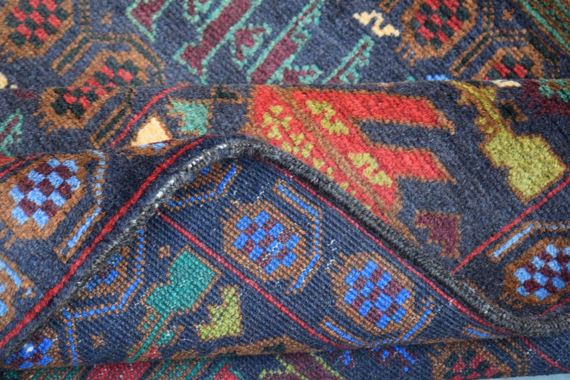A handmade Afghan wool rug featuring a dark blue background with geometric and floral patterns.