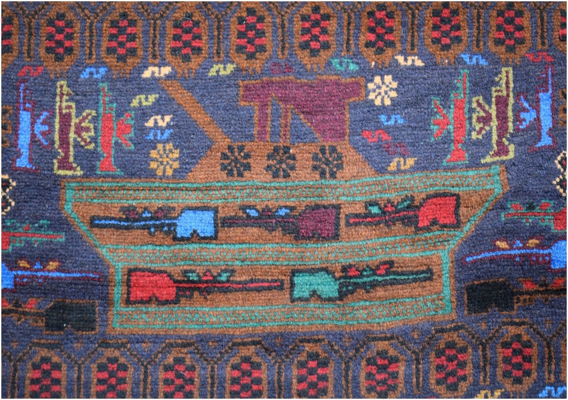 Handmade Afghan wool rug featuring a woven tank and rifle motifs on a dark blue background.