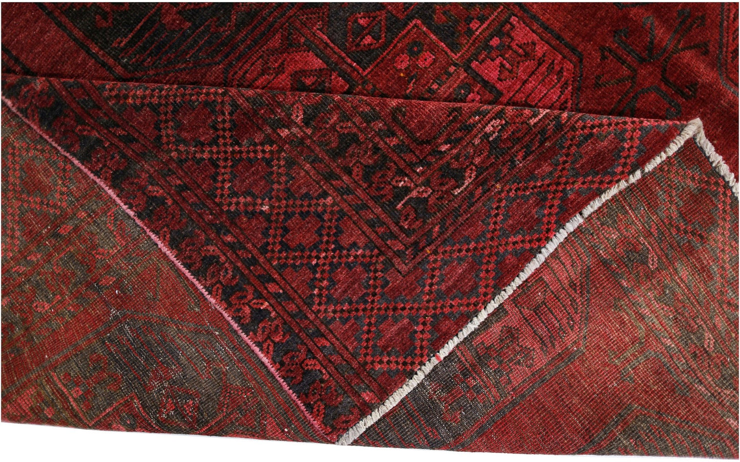 A folded antique Afghan Turkmen rug featuring a deep red background and geometric patterns.