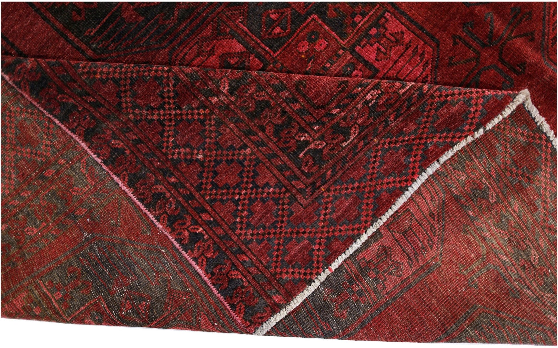 A folded antique Afghan Turkmen rug featuring a deep red background and geometric patterns.