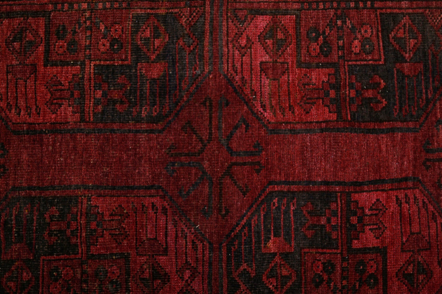 An antique Afghan Turkmen rug featuring a deep red background with black geometric elephant foot motifs.