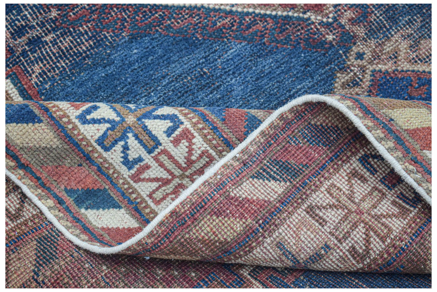 A handwoven antique Persian rug with a blue and red geometric pattern, shown folded.