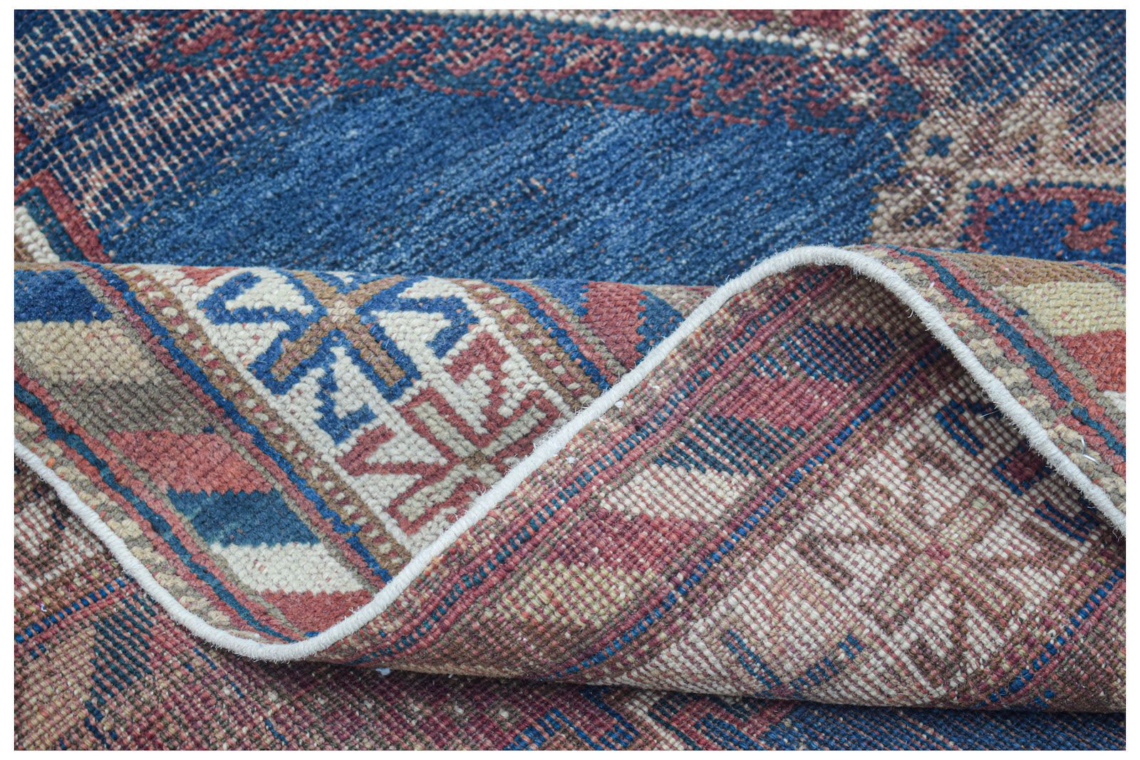 A handwoven antique Persian rug with a blue and red geometric pattern, shown folded.