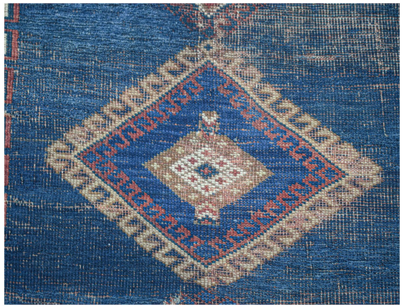 An antique Persian rug featuring a central diamond medallion in blue, red, and cream tones.