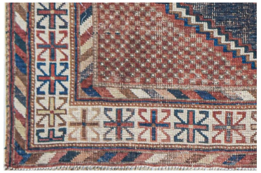 A corner view of an antique handwoven Persian rug featuring geometric patterns in red and blue.