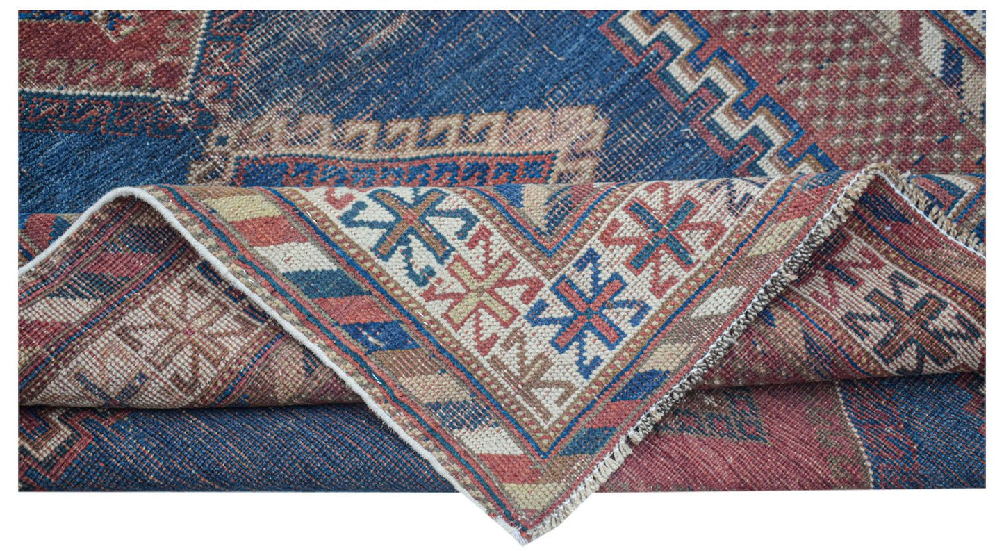 An antique Persian rug featuring a blue field with geometric patterns and a folded corner.