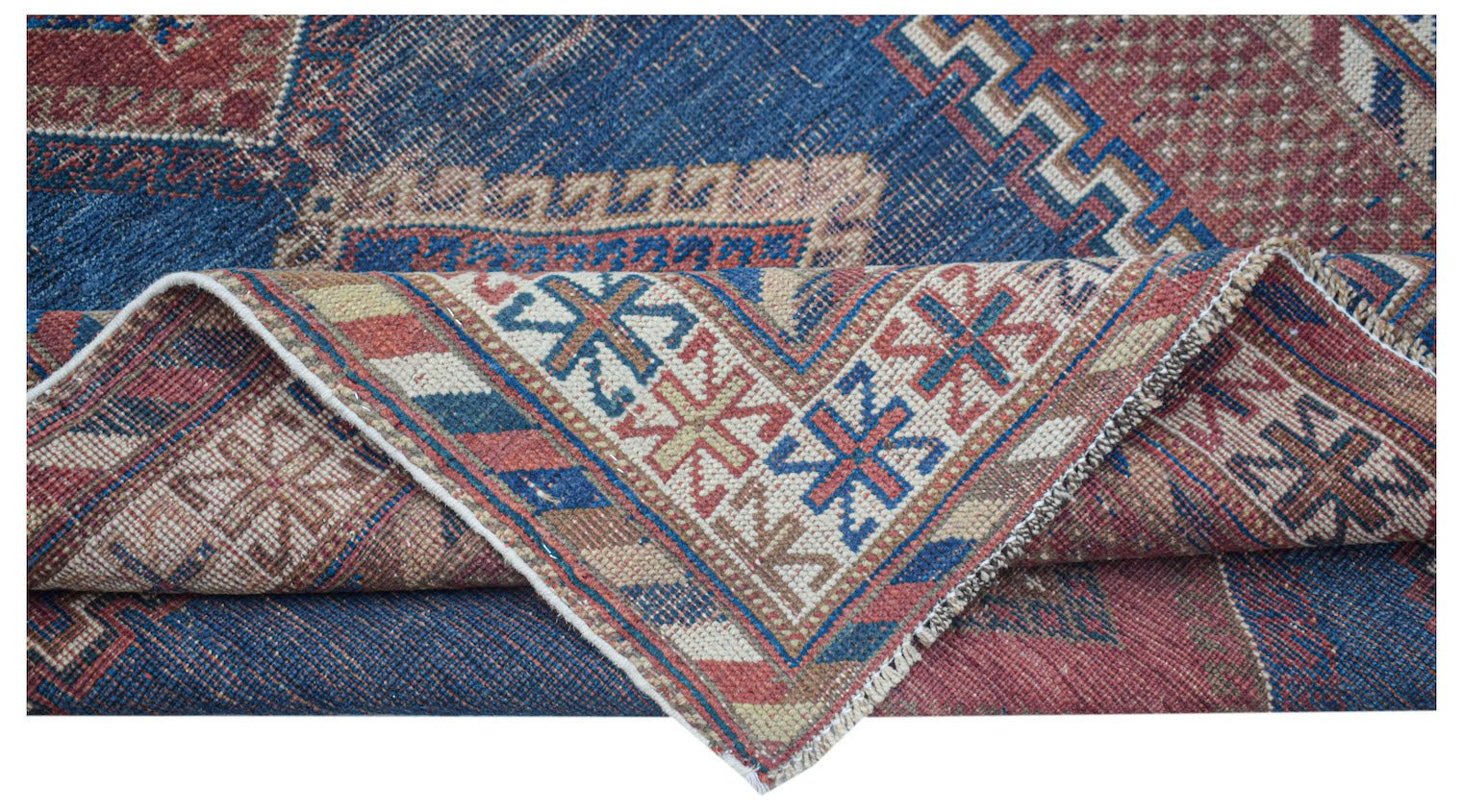 An antique Persian rug featuring a blue field with geometric patterns and a folded corner.