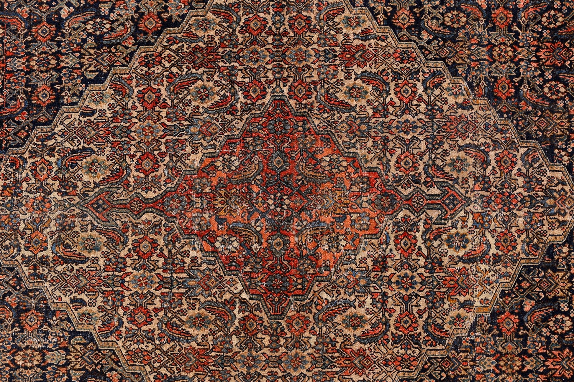 An antique Persian Senneh rug featuring a detailed geometric medallion in red, blue, and beige.