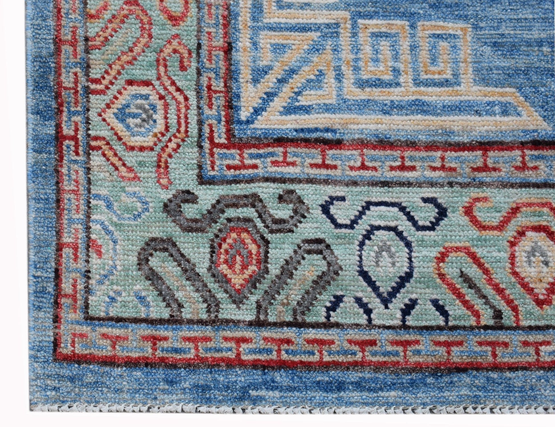 A corner detail of a handwoven Afghan Chobi rug featuring intricate geometric and floral patterns.