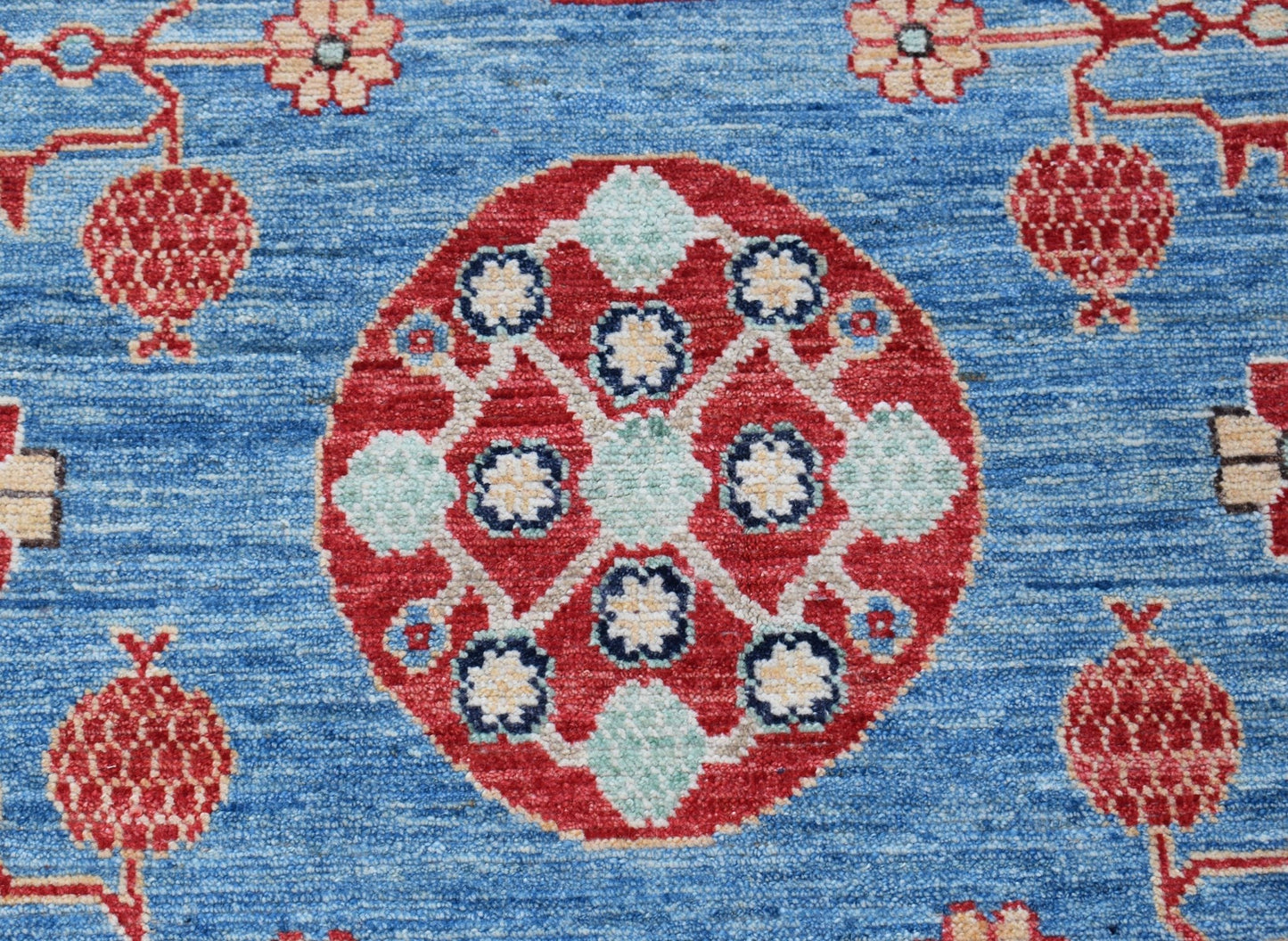 A handmade Afghan Chobi rug featuring a central red medallion with floral motifs on a blue field.