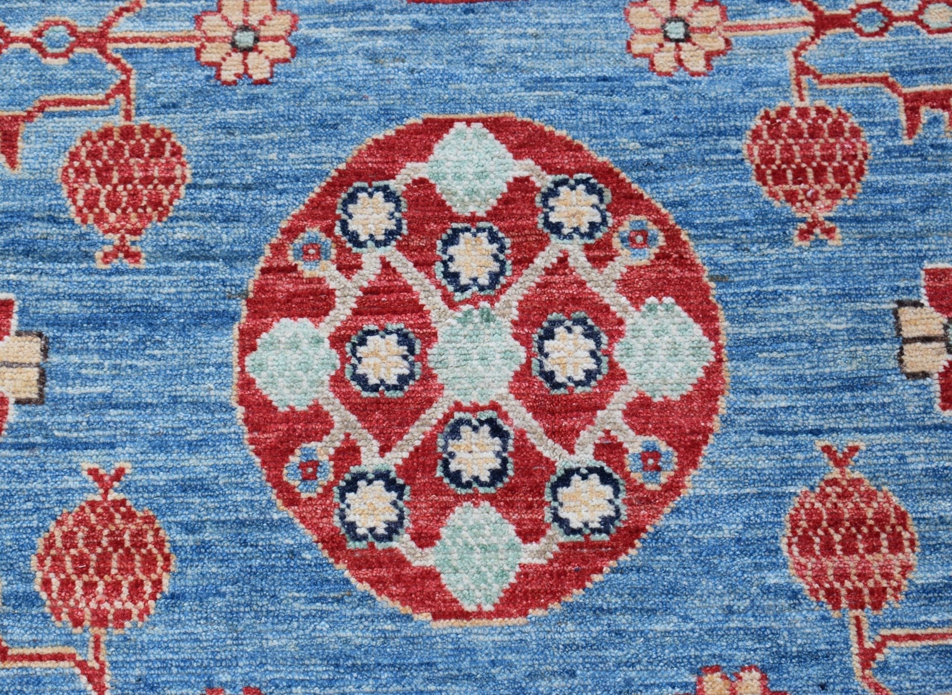 A handmade Afghan Chobi rug featuring a central red medallion with floral motifs on a blue field.