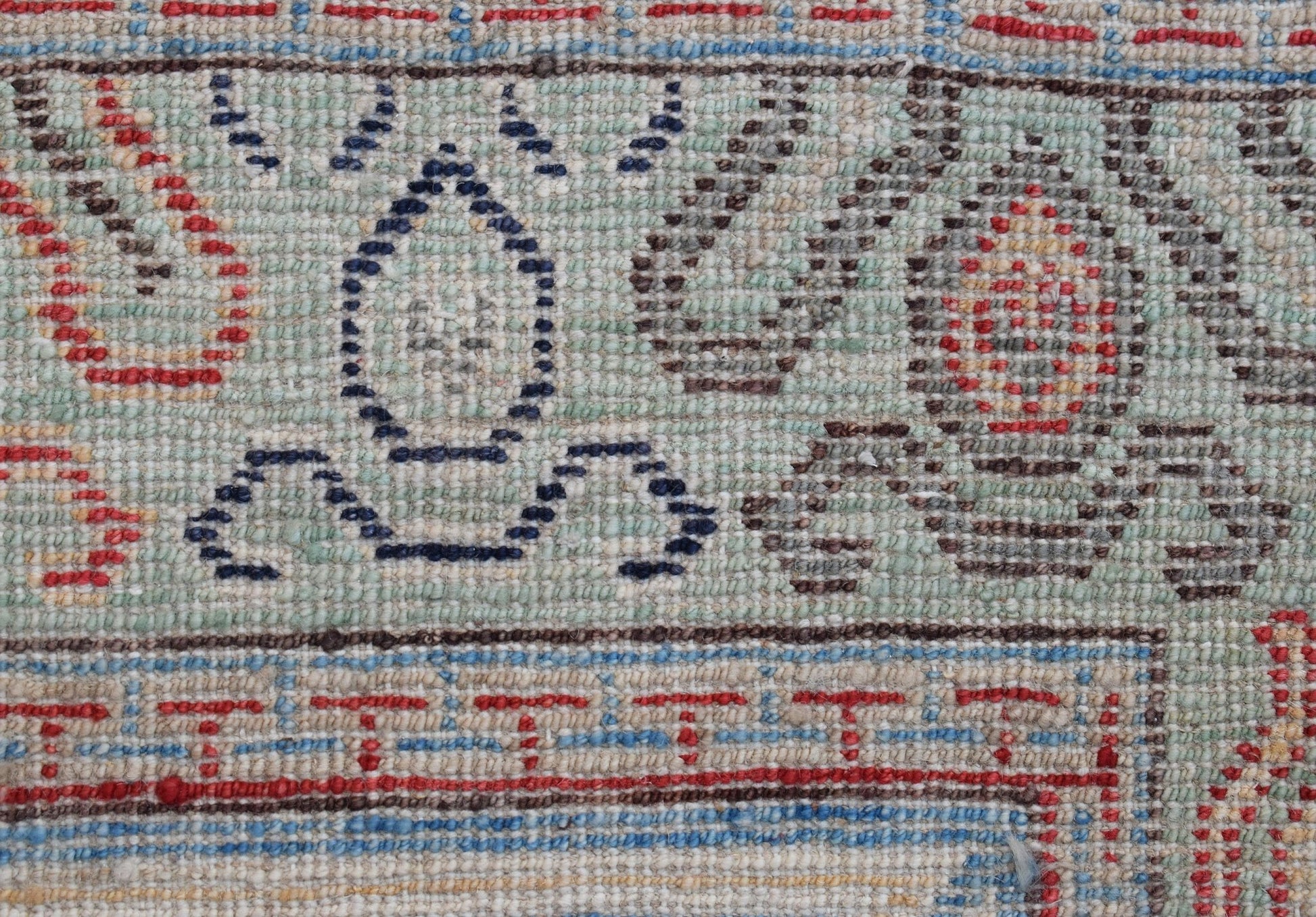 A close-up of a handwoven Afghan Chobi rug featuring traditional geometric patterns in blue and red.