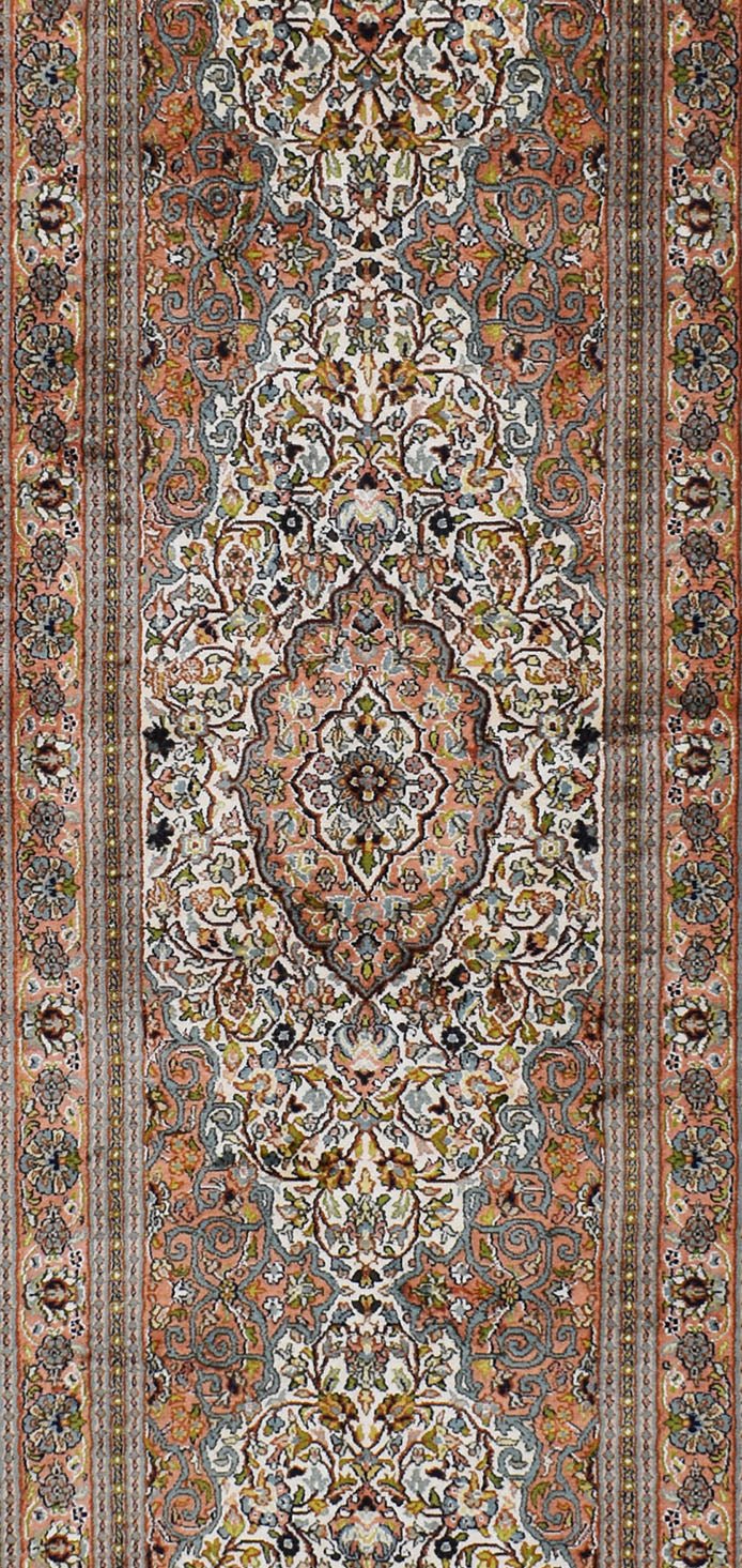 A handmade Kashmiri silk runner featuring an intricate floral Persian pattern in peach and blue.
