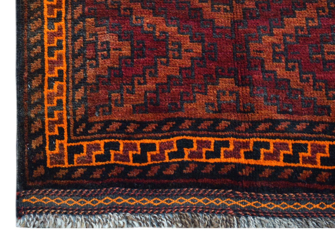 A vintage handmade Afghan Baluch wool rug featuring geometric patterns in red, orange, and black.