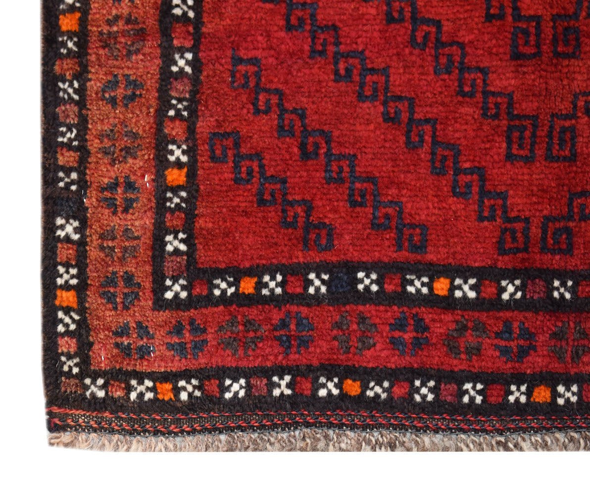 A close-up of a vintage Afghan Baluch rug featuring geometric patterns in red and dark blue wool.
