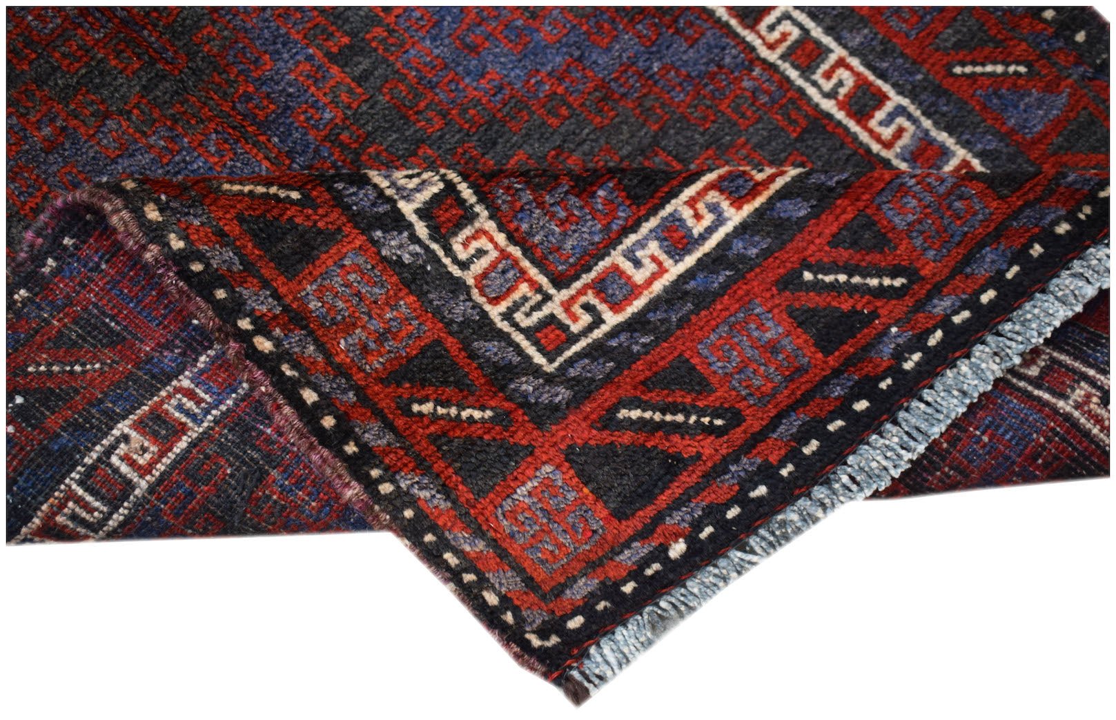 A folded vintage Afghan Baluch rug featuring geometric patterns in dark red, blue, and ivory wool.