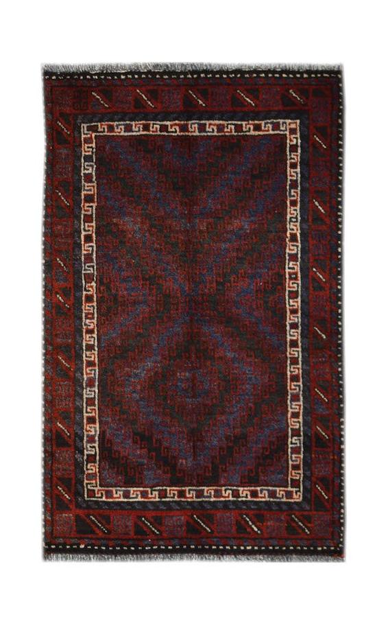 A handmade vintage Afghan Baluch rug featuring a geometric pattern in dark red, blue, and brown.