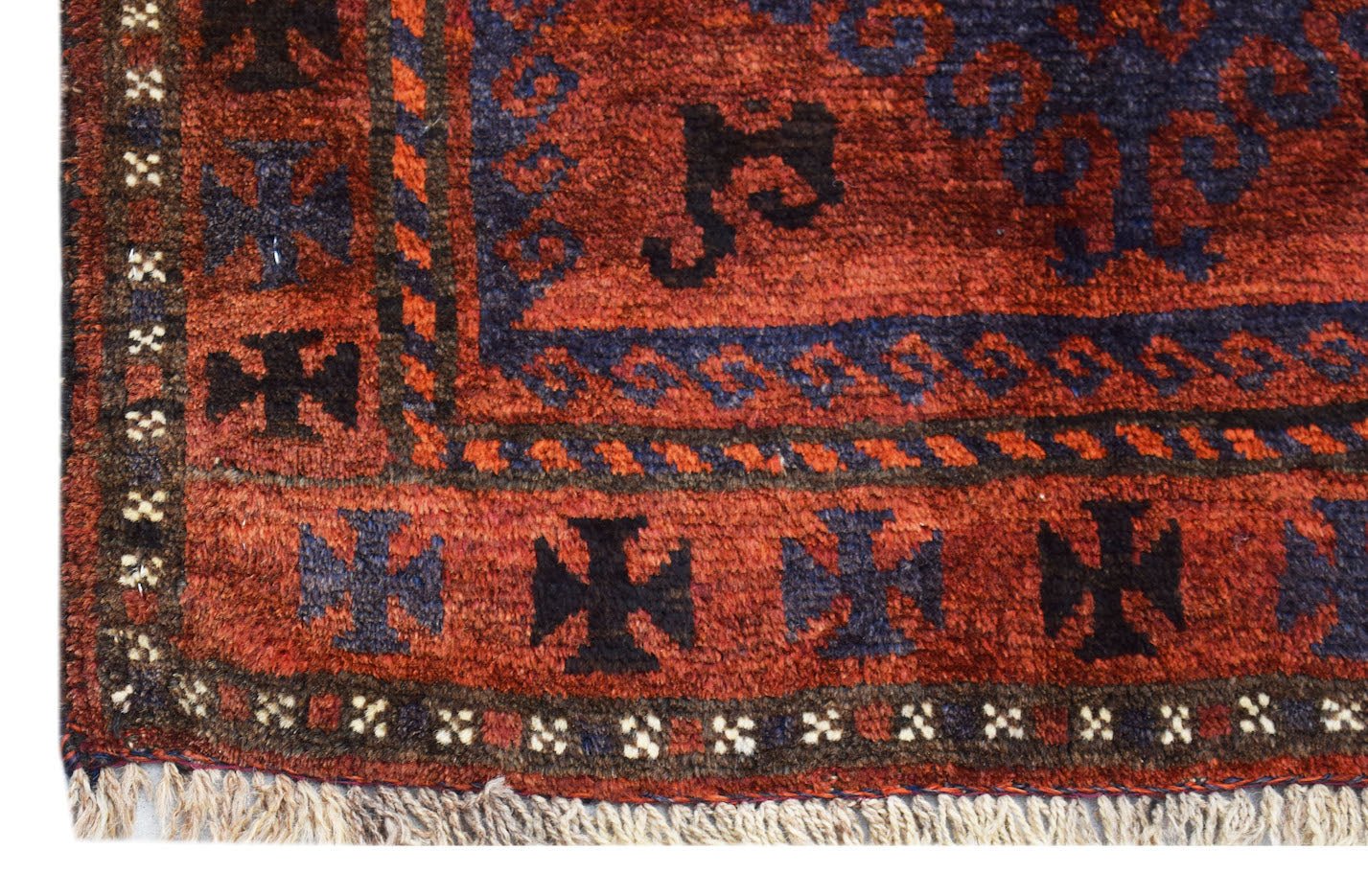 A vintage handmade Afghan Baluch rug featuring a dark red field with blue cross motifs and fringe.