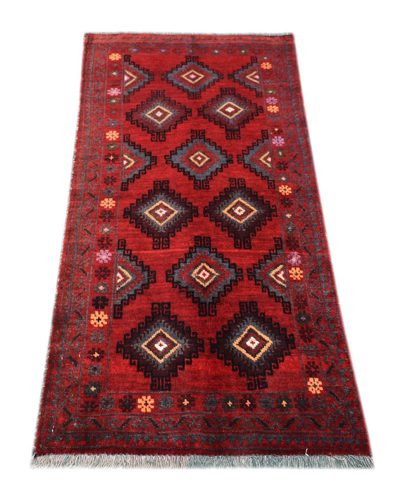 A vintage handmade Afghan Baluch rug featuring a red field with repeating diamond motifs.