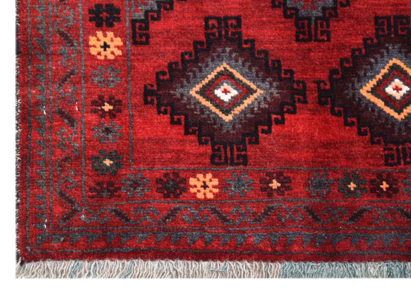 A vintage handmade Afghan Baluch rug featuring geometric diamond patterns in red and dark tones.
