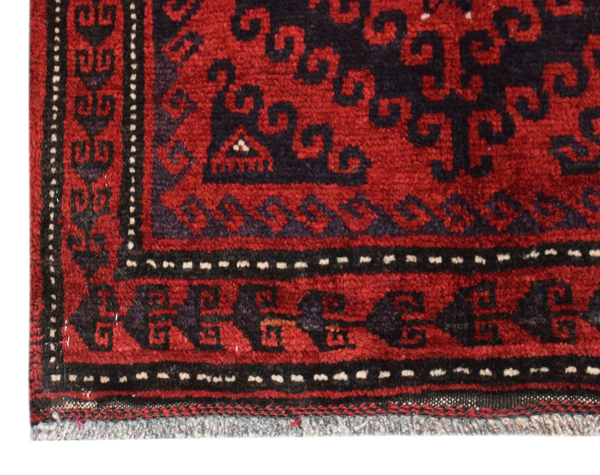 A close-up of a vintage Afghan Baluch rug featuring traditional geometric patterns in red and black.