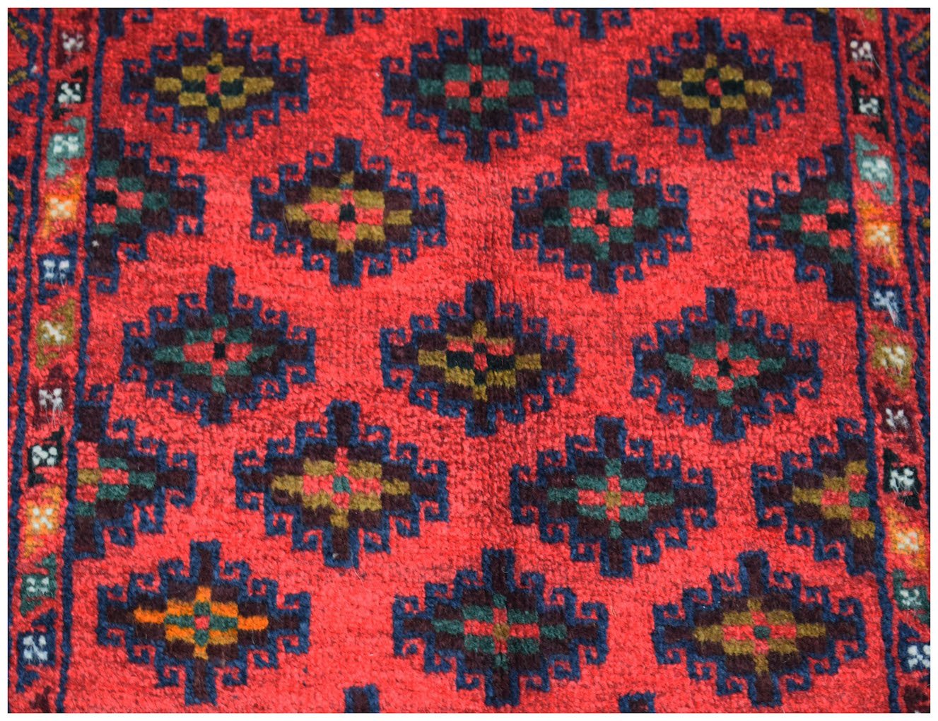 A vintage Afghan Baluch wool rug featuring a repeating geometric diamond pattern in red and blue.
