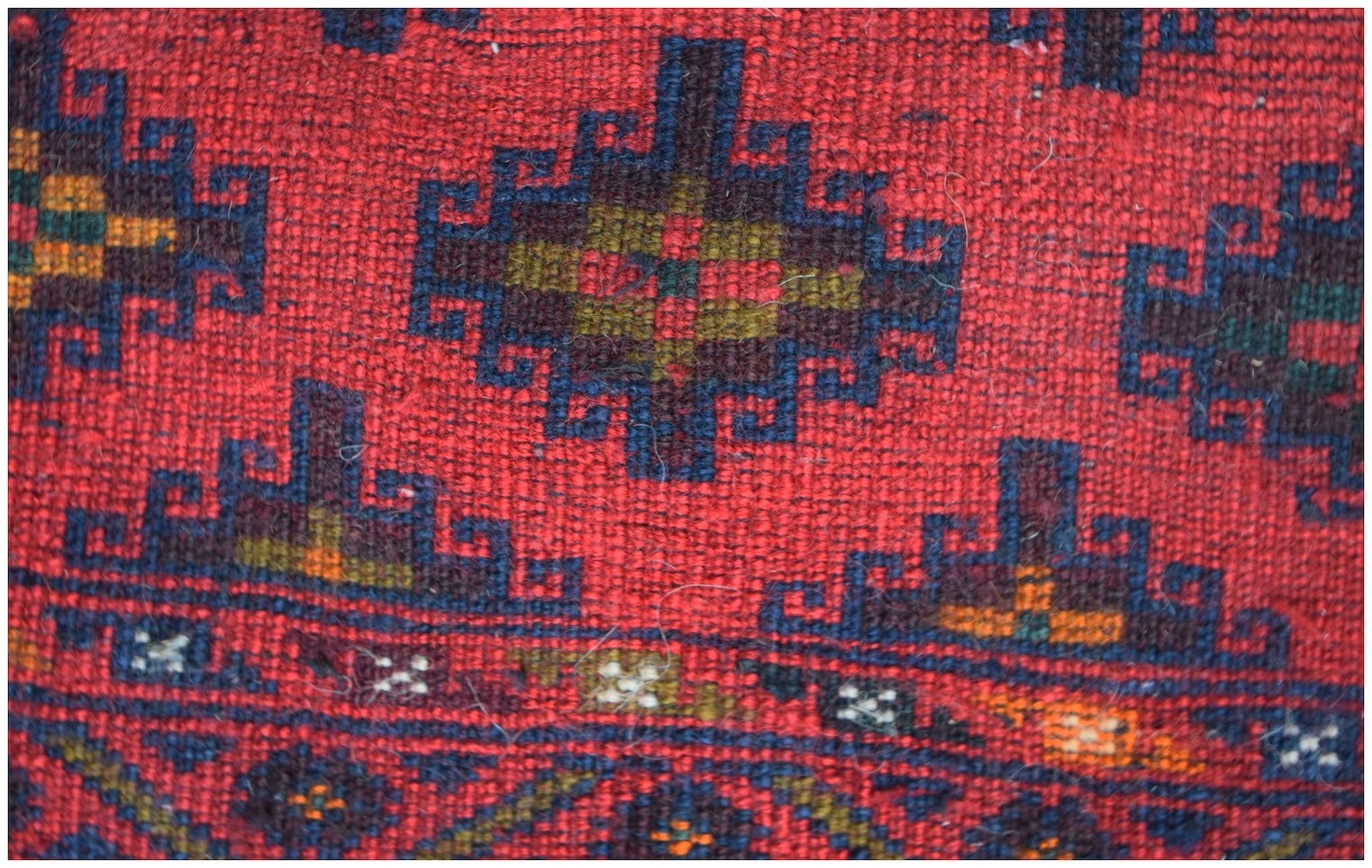 A close-up of a vintage Afghan Baluch rug featuring geometric patterns in red, blue, and gold.