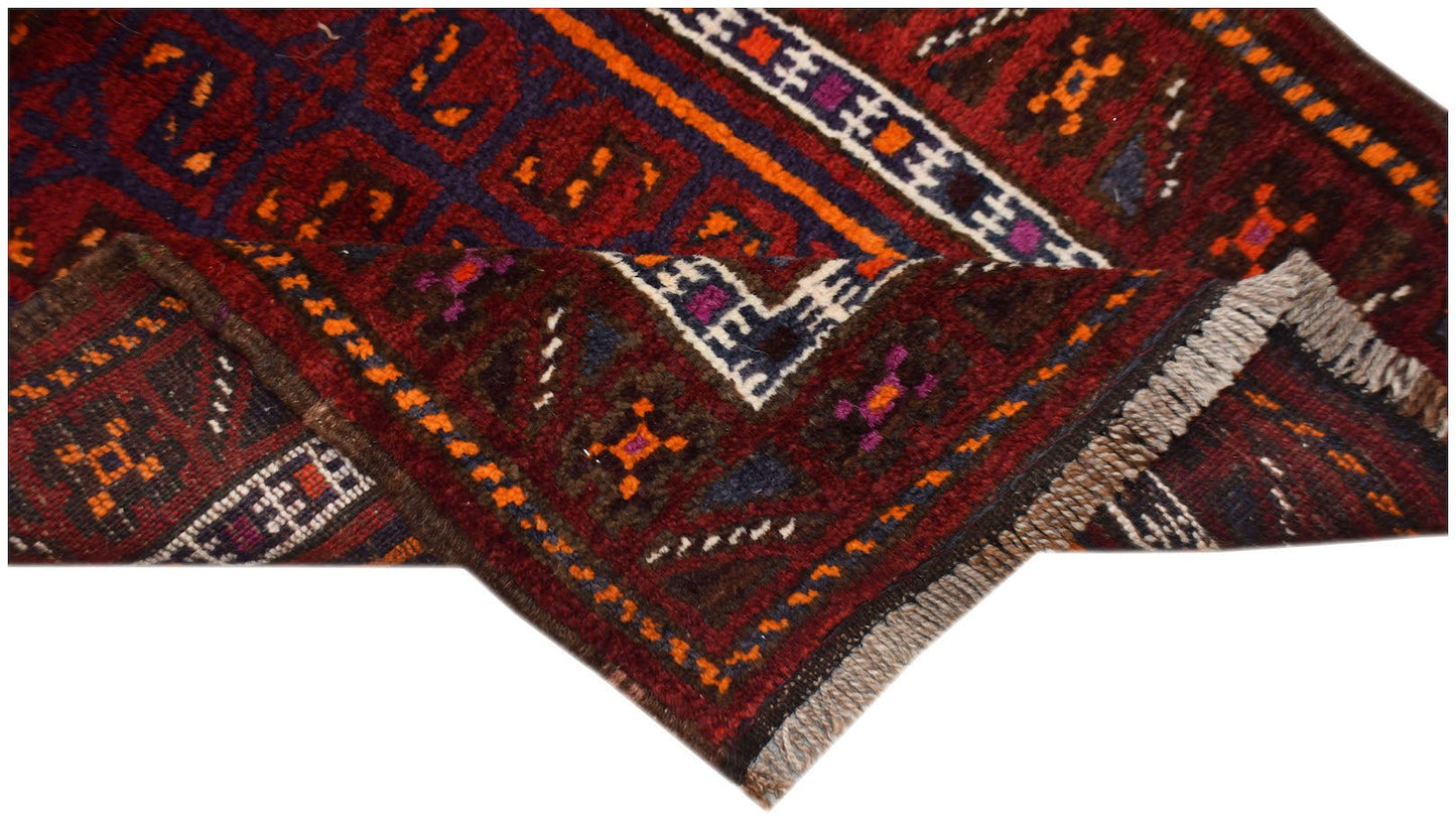 A vintage handmade Afghan Baluch wool rug featuring geometric patterns in deep red and orange tones.