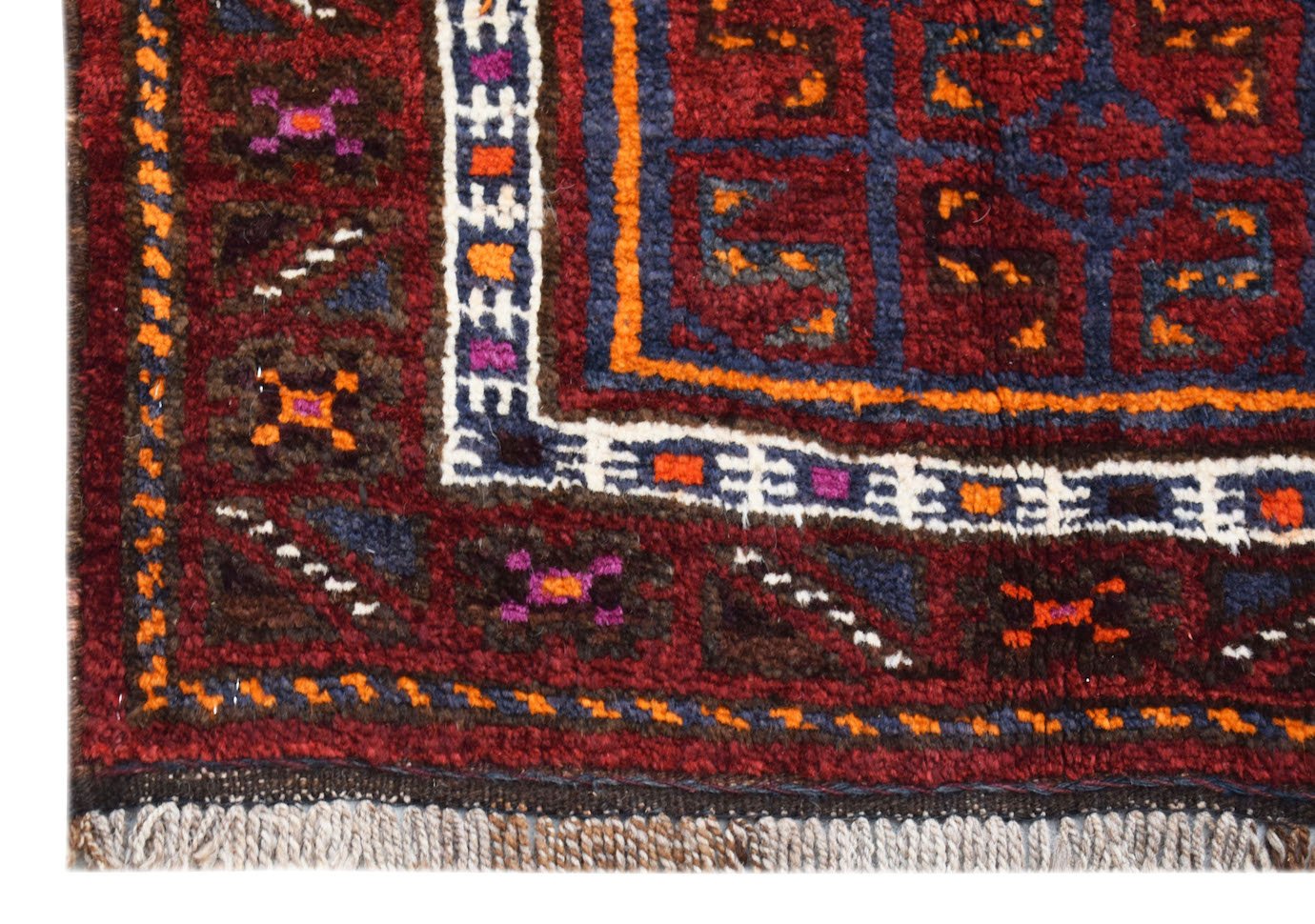 A corner view of a vintage Afghan Baluch wool rug featuring geometric patterns in red and blue.